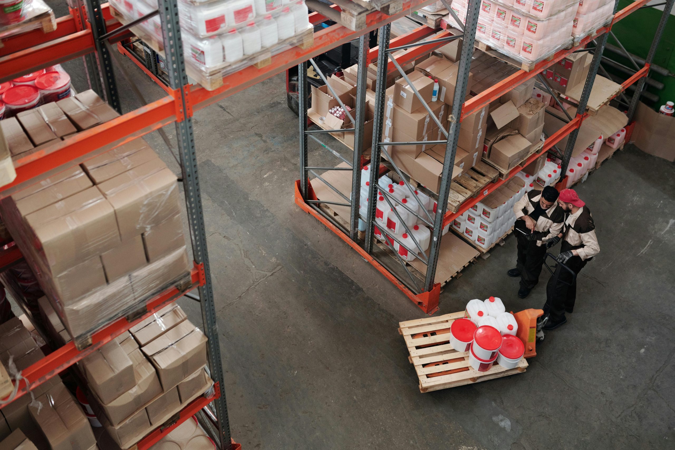 Workers managing inventory on shelves in a warehouse, viewed from above.